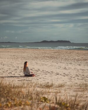 Persona meditando en la playa al amanecer conectando con la energía del océano
