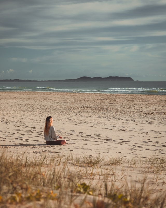 Persona meditando en la playa al amanecer conectando con la energía del océano